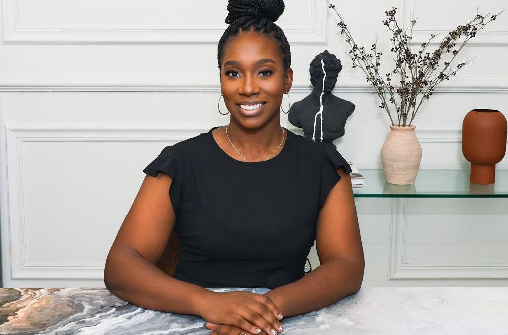 Smiling woman in black top sitting at desk with modern decor in the background.