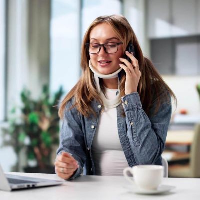 a woman sitting at a table talking on a cell phone, she has a neck brace