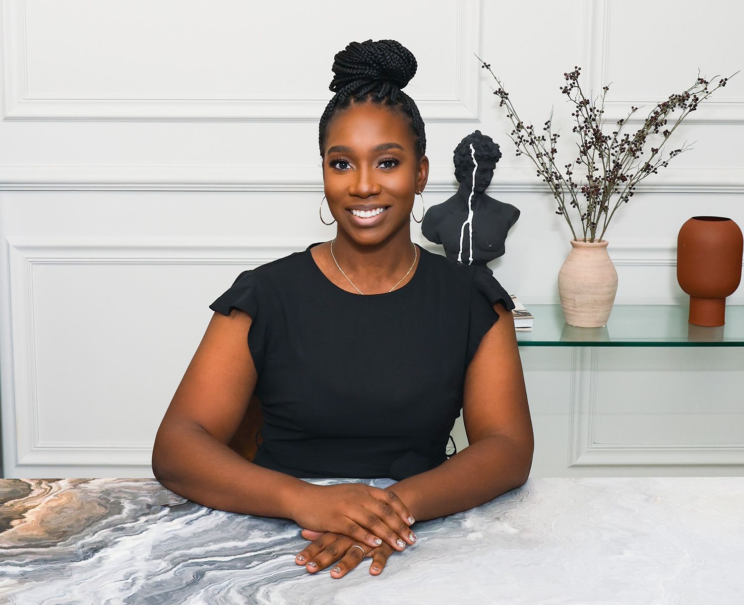 Smiling woman in black top sitting at desk with modern decor in the background.