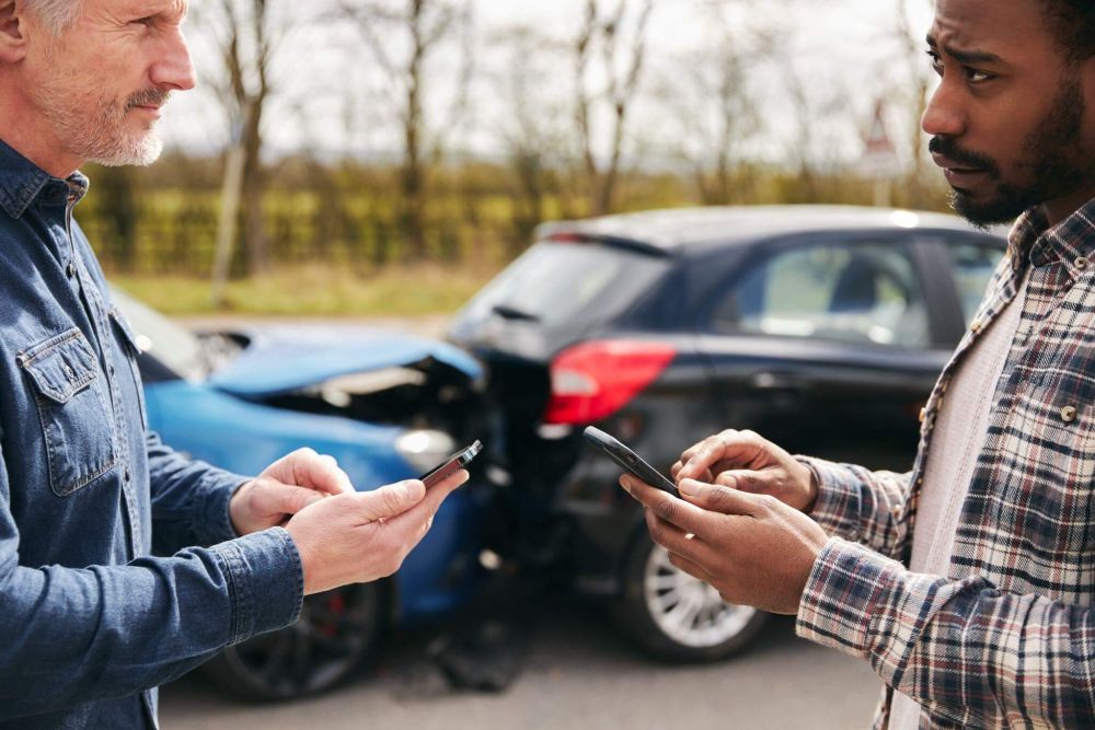 two men standing next to each other looking at their cell phones