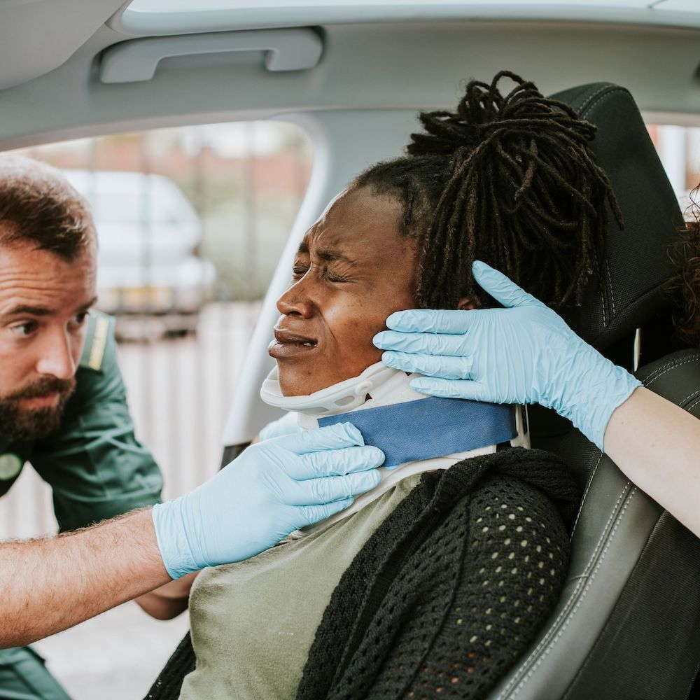 Paramedics assisting an injured person with a neck brace after a car accident.