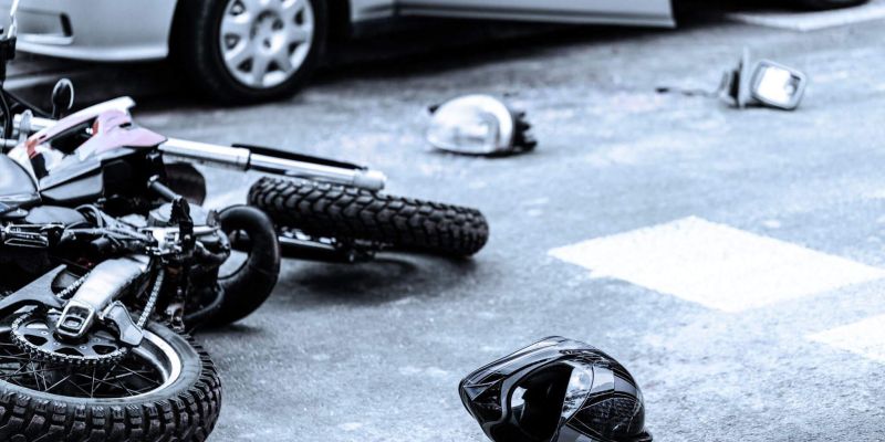 Fallen motorcycle on asphalt next to debris and a parked car