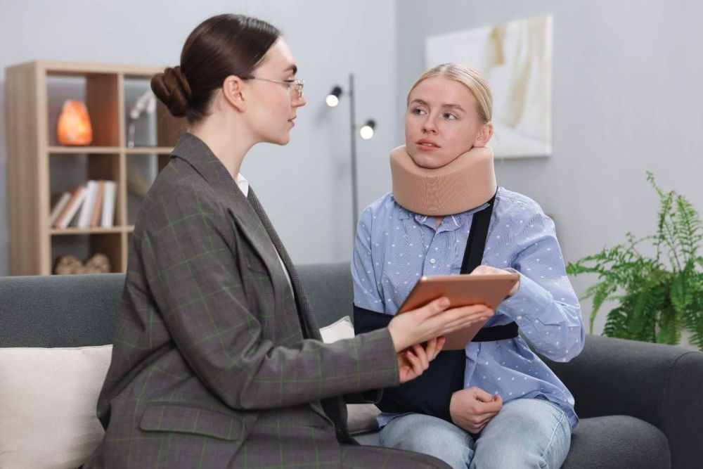 a woman sitting on a couch talking to another woman, one of them is wearing a neck brace