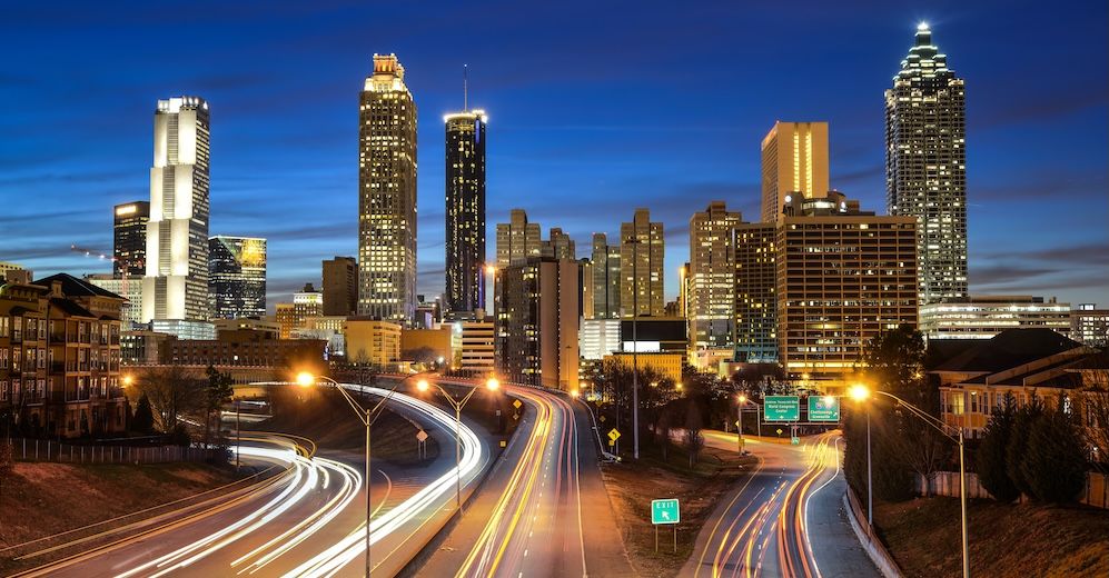 Atlanta city skyline at night with illuminated skyscrapers and light trails from traffic on highways.