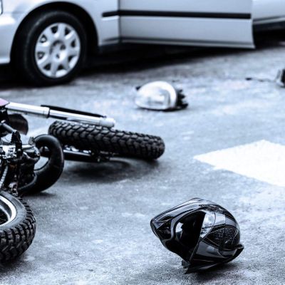 Fallen motorcycle on asphalt next to debris and a parked car