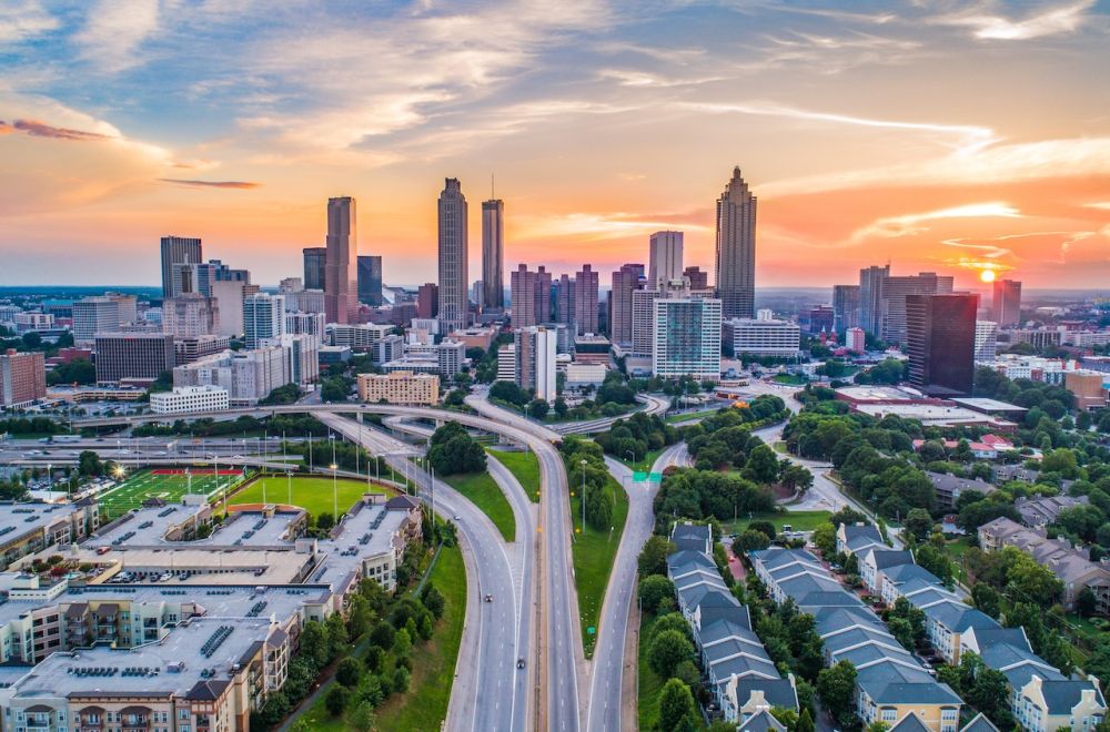 Aerial view of Atlanta skyline at sunset, showcasing tall buildings and highways under a colorful sky.