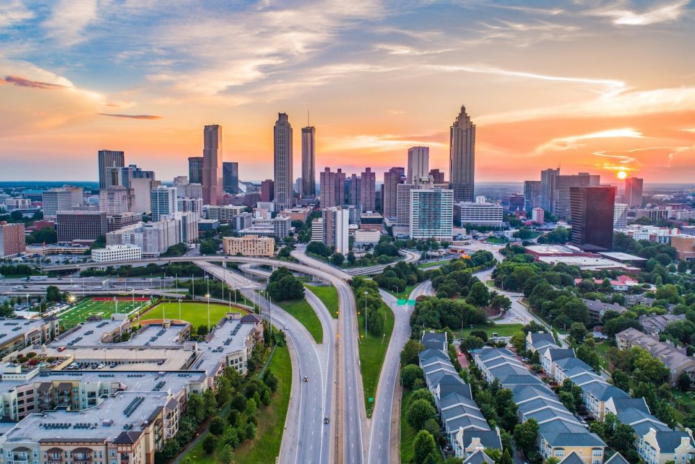Aerial view of Atlanta skyline at sunset, showcasing tall buildings and highways under a colorful sky.