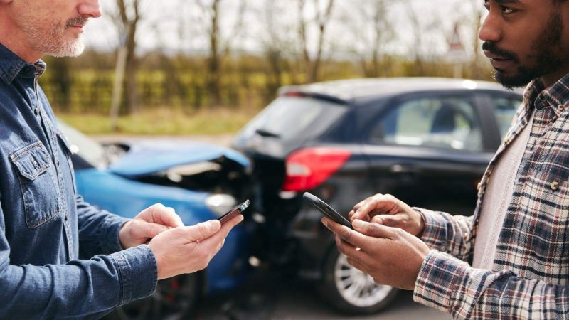 two men standing next to each other looking at their cell phones