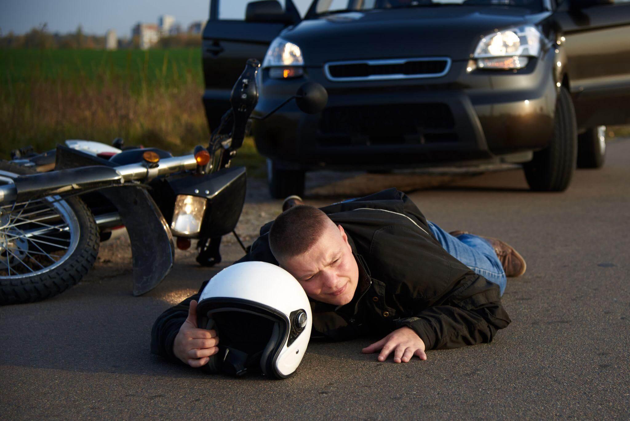 A man lying by a motorcycle after an accident, there's a car in the background