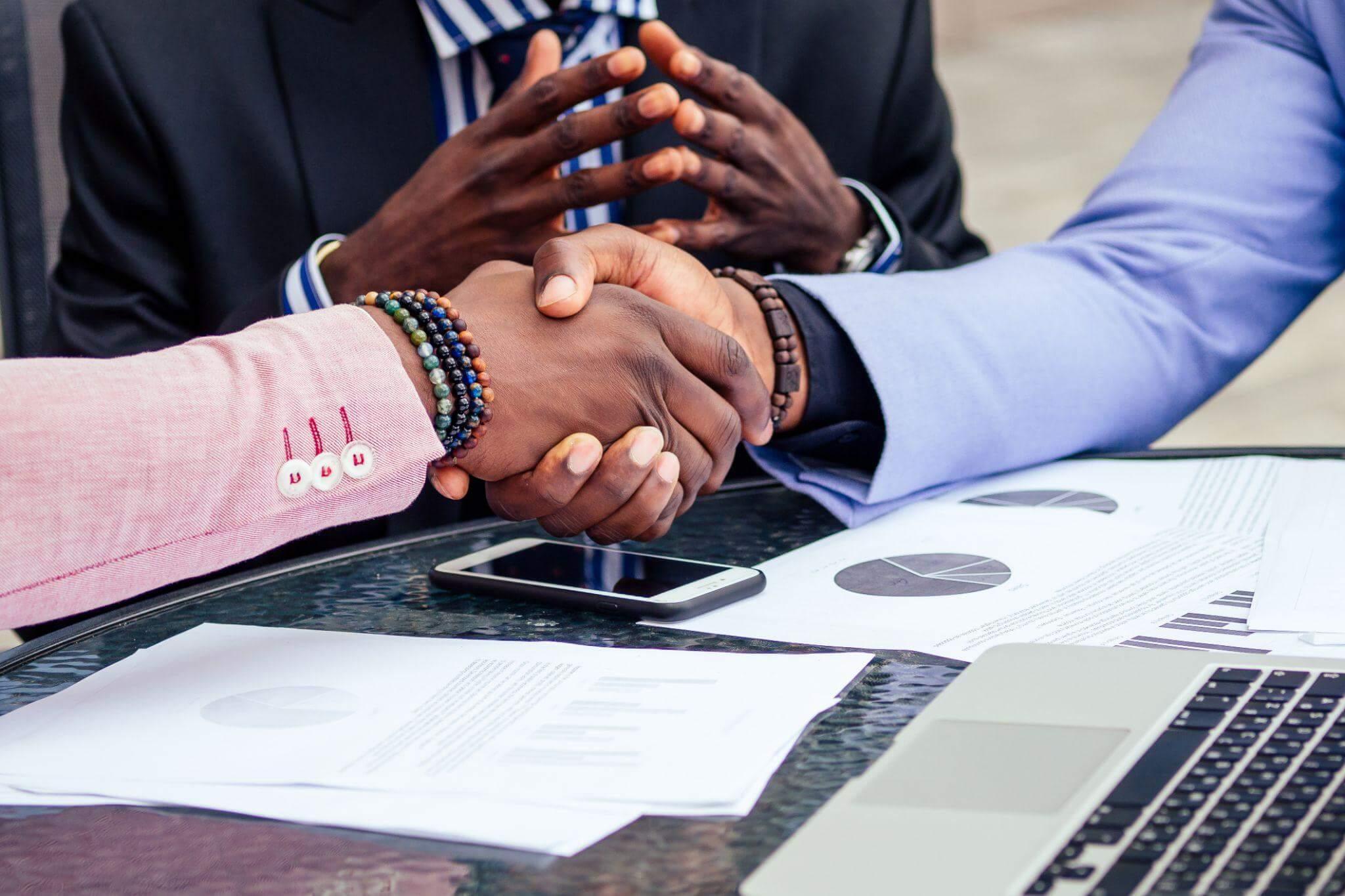 two men shaking hands over a laptop computer